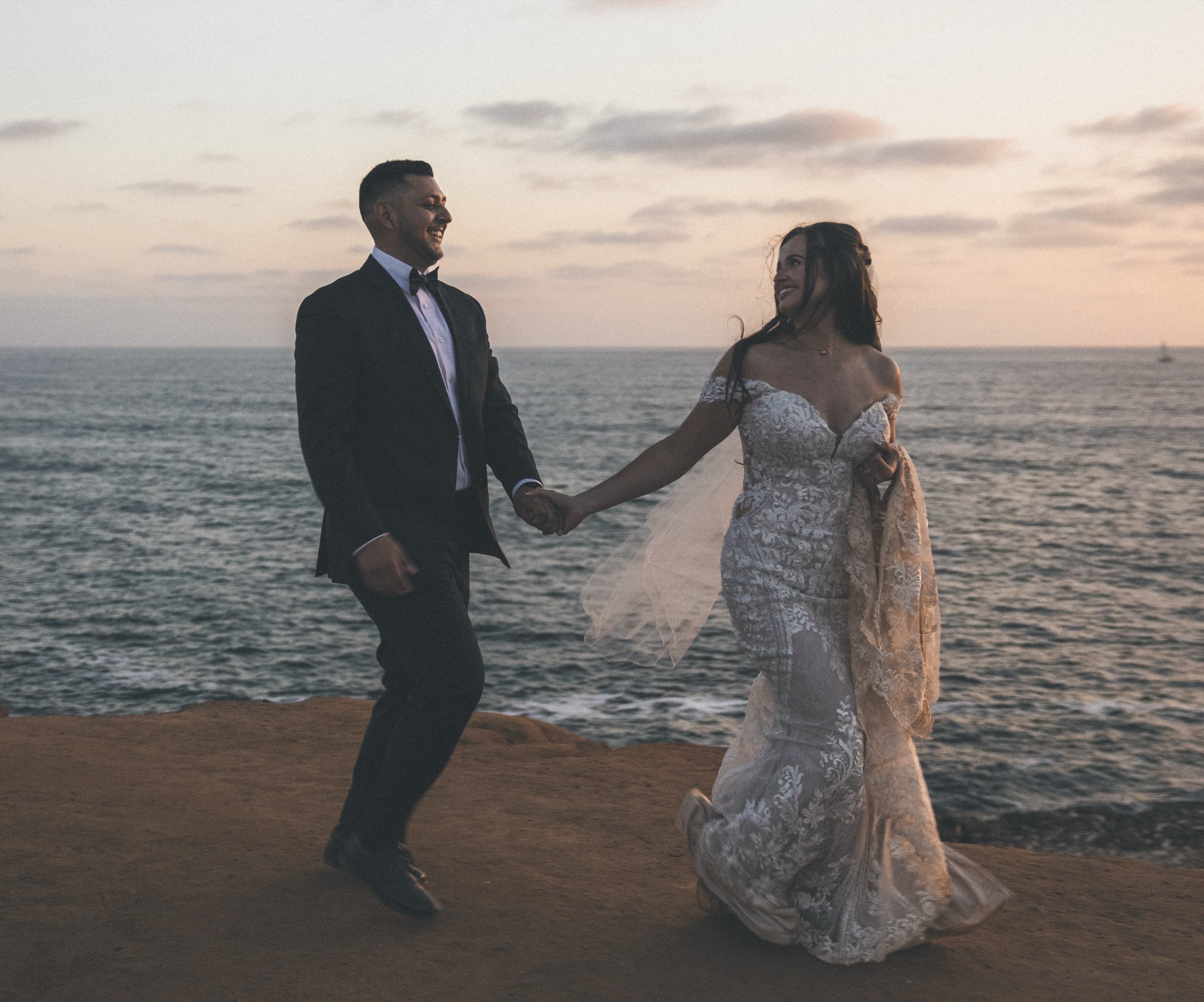 Bride and groom laughing and holding hands at golden hour by the sea