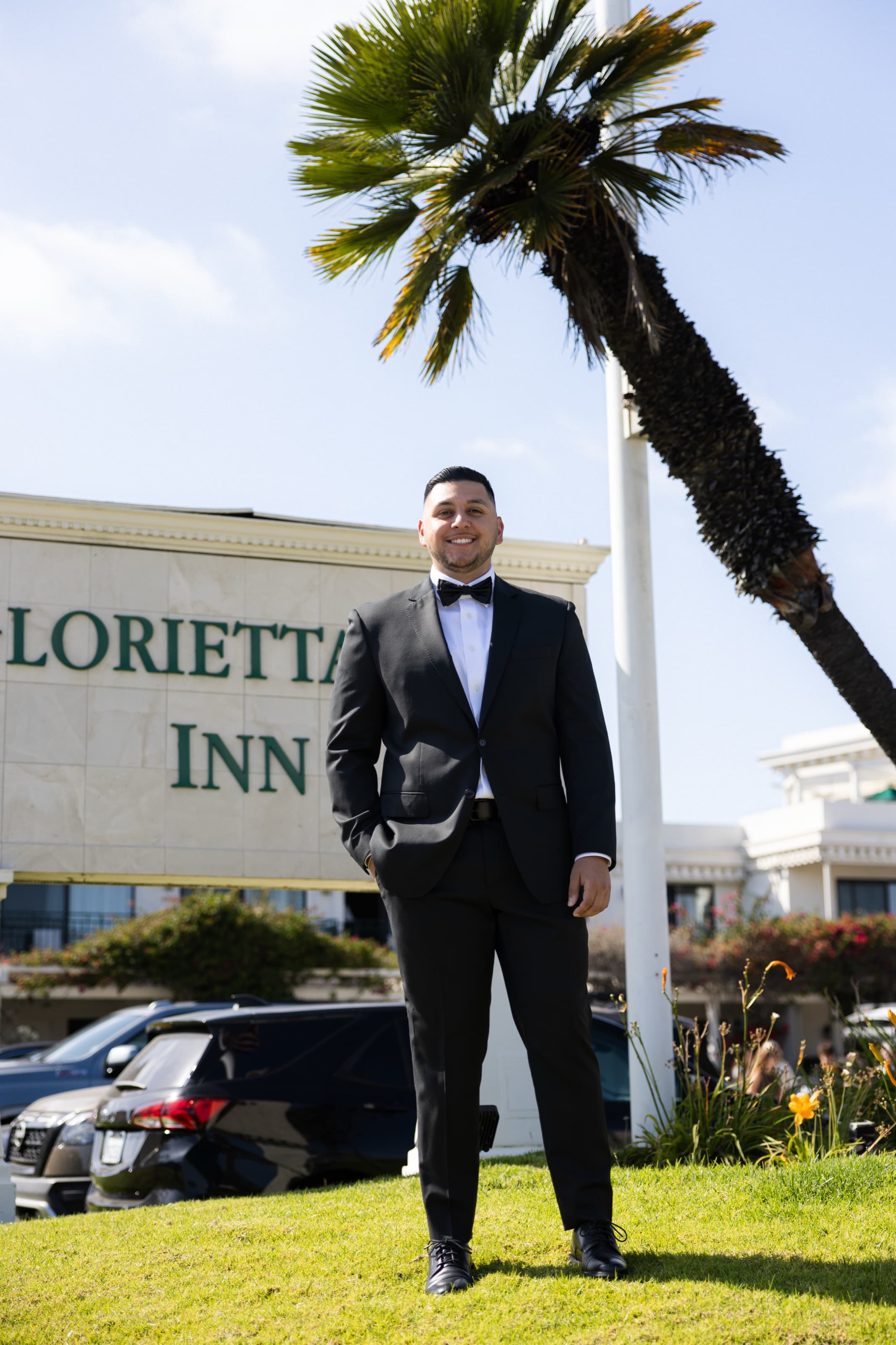 Groom in a tux smiling outside a Coronado hotel under a palm tree