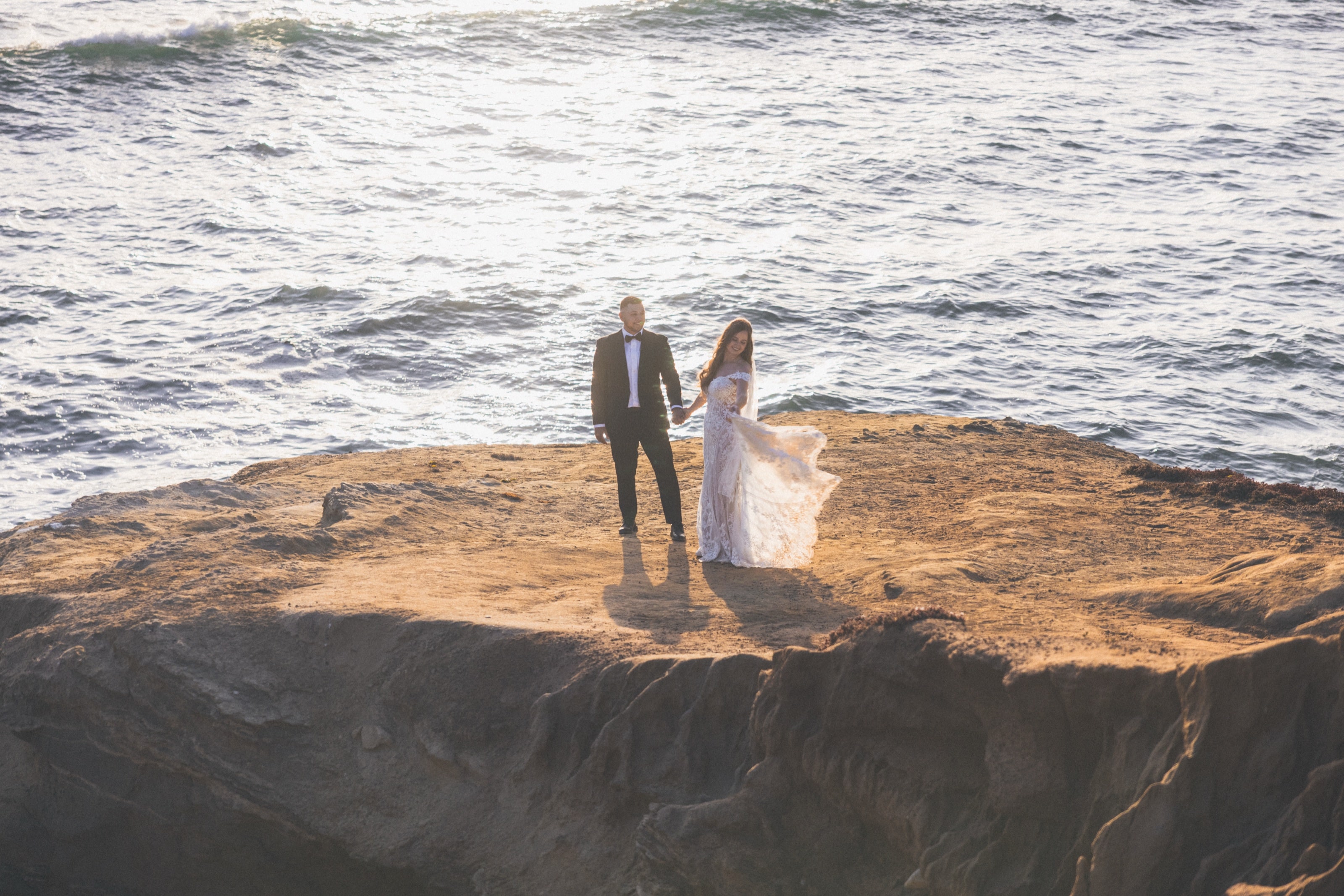 Bride and groom holding hands on a sunset cliff above the Pacific in San Diego