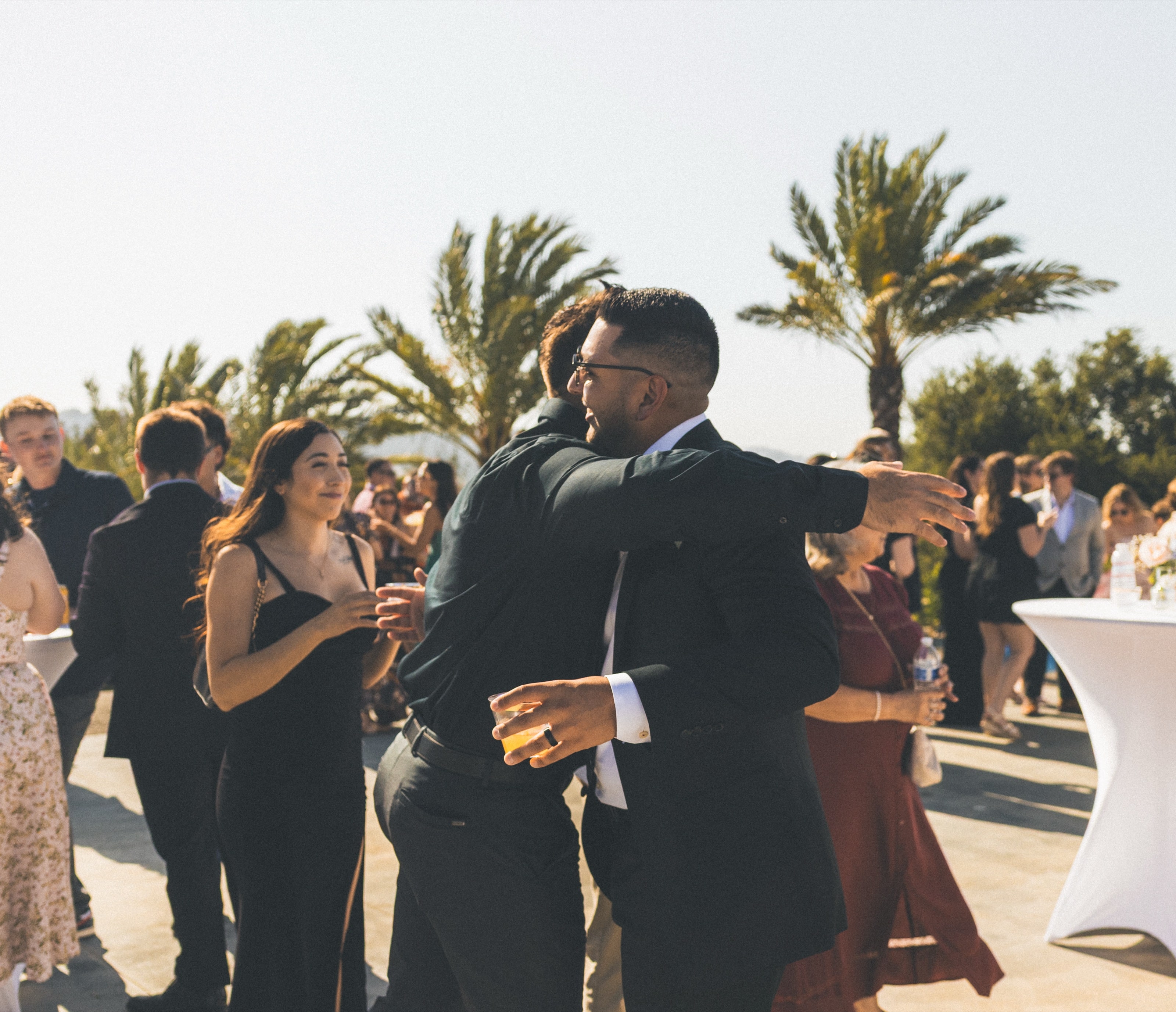 Guests hugging at a sunny cocktail hour under palm trees